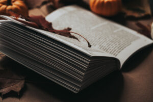 Livre ouvert avec feuille d'érable posée dessus, et entouré de petits potimarrons.