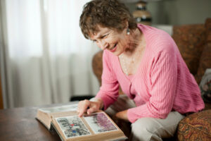 Femme âgée qui regarde un album photos en souriant.