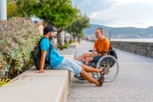 Adulte en fauteuil roulant qui discute gaiement avec un ami, au bord de la mer.