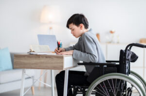 Enfant en fauteuil roulant qui fait ses devoirs à son domicile.