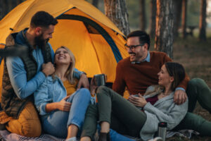 Deux couples d'amis qui ont un fou rire devant une tente jaune de camping.