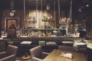 Bar restaurant à l'ambiance contemporaine et chaleureuse avec une lumière tamisée et des bouteilles accrochées en hauteur via des câbles.