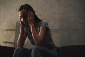 Jeune femme triste assise sur un canapé la tête dans les mains.