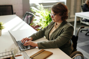 Femme en fauteuil roulant à un bureau et qui tape un texte à l'ordinateur.