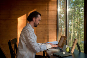 Homme assis à son bureau et qui tape un texte à l'ordinateur dans une pièce au calme avec vue sur la nature.