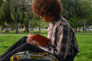 Jeune femme assise dans un parc entouré de verdure et qui écrit dans un cahier.