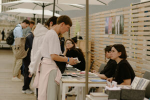 Salon du livre lors duquel une personne parcourt le livre d'une autrice assise à un stand.