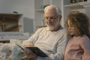 Grand-père assis sur un canapé avec sa petite fille et qui lui lit son autobiographie.