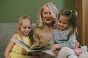 Grand-mère qui lit son autobiographie à ses deux petites-filles, toutes les trois assises sur un canapé, l'une des petites-filles sur les genoux de sa grand-mère.