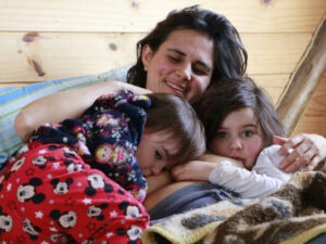 Femme souriante couchée dans un lit et qui fait des câlins à son fils et sa fille encore petits.